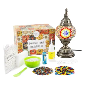 A Turkish mosaic lamp kit with a bronze base, colorful glass tiles, beads, glue, and instructions laid out on a workspace — designed for hands-on DIY assembly.