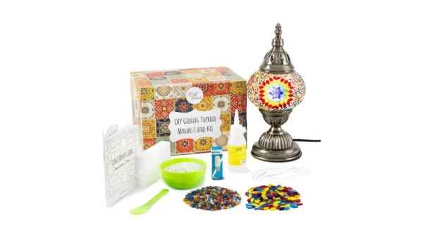 A Turkish mosaic lamp kit with a bronze base, colorful glass tiles, beads, glue, and instructions laid out on a workspace — designed for hands-on DIY assembly.