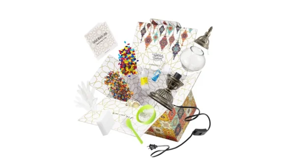 A Turkish mosaic lamp kit with a bronze base, colorful glass tiles, beads, glue, and instructions laid out on a workspace — designed for hands-on DIY assembly.