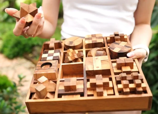 Person holding a handcrafted wooden puzzle piece with the full 16-piece wooden puzzle box visible.