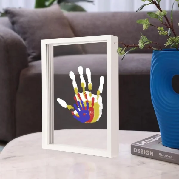 Colorful overlapping handprints of an adult and child displayed in a transparent frame on a coffee table.