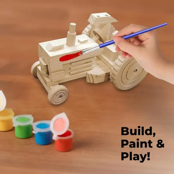 Child’s hand painting a wooden tractor model with red paint and a blue paintbrush, with open paint pots in various colors nearby.