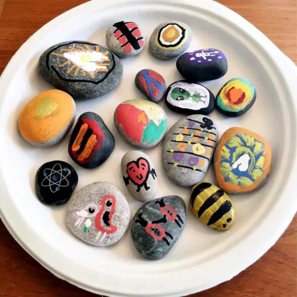 A collection of creatively painted rocks displayed on a white plate, featuring abstract and cartoon designs.