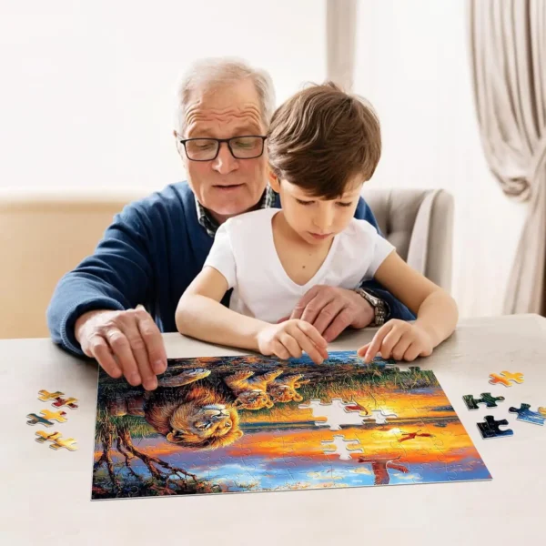 Elderly man and young boy assembling a colorful wildlife puzzle featuring lions at sunset on a table.
